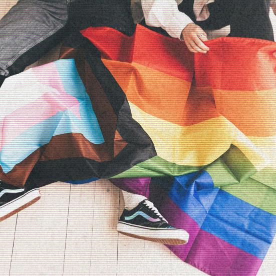 En person sidder med et Pride-flag viklet omkring sig; sneakers og flagets farver fylder billedet.