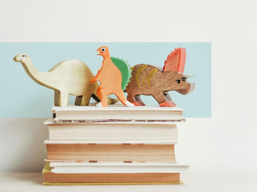 Tre dinosaur-træfigurer står oven på en stak bøger.